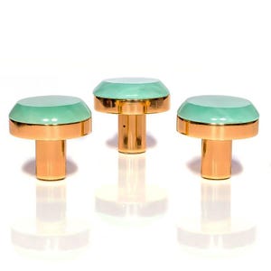 Può includere: Tre pomelli decorativi per mobili con base dorata e parte superiore verde menta. I pomelli hanno una forma arrotondata, a forma di fungo, e sono su uno sfondo bianco. I pomelli sono probabilmente in metallo e vetro.