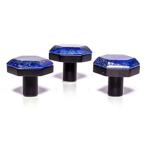 May include: Three cabinet knobs with a decorative design. Each knob has an octagonal top with a blue and gold pattern, set on a black base and stem. The knobs are displayed against a white background.