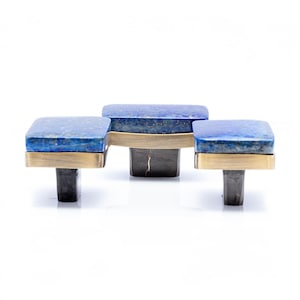 Peut inclure: Ensemble de trois poignées de meubles. Chaque poignée présente un dessus carré en lapis-lazuli bleu avec des détails en laiton. Montées sur des tiges en métal gris foncé, elles ajoutent une touche élégante.