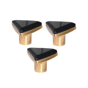 Puede incluir: Tres tiradores de armario con una parte superior triangular negra, un marco color latón y una base cilíndrica color latón. Los tiradores están dispuestos en un patrón triangular sobre un fondo blanco. Adecuado para muebles y decoración del hogar.