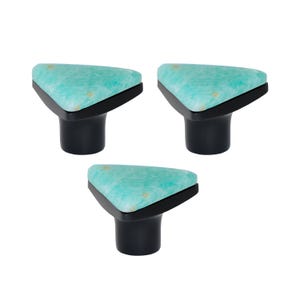 Puede incluir: Tres tiradores de armario con una parte superior triangular con un patrón turquesa y dorado. Los tiradores tienen un borde negro y una base cilíndrica negra. Estos tiradores decorativos son adecuados para muebles.