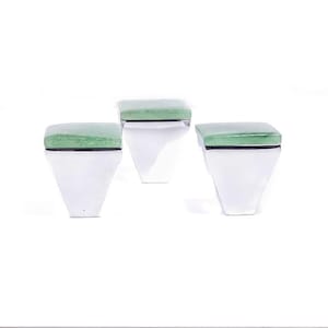 May include: Three contemporary decorative boxes. Each box features a white, trapezoid-shaped base and a square, light green top. A thin black line separates the top and base. The boxes are set against a white backdrop.
