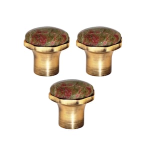 May include: Three cabinet knobs with a natural stone top in shades of green and red, set on a brass-coloured base. The knobs have a rounded, mushroom-like shape, ideal for adding a touch of nature to furniture.