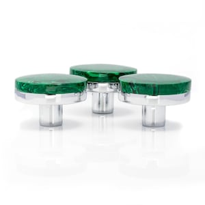 May include: Three decorative cabinet knobs. Each knob has a round, marbled green top with a silver band and a cylindrical silver base. The knobs are set against a white background, creating a clean and modern aesthetic.