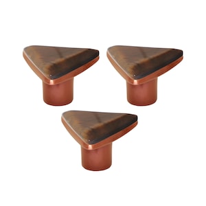 May include: Three cabinet knobs with a triangular top and a copper-coloured base. The top has a dark brown, wood-grain appearance. The knobs are arranged in a triangular pattern against a white background.