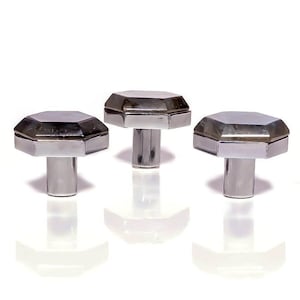 May include: Three silver cabinet knobs are shown against a white backdrop. Each knob features an octagonal top and a cylindrical stem. The knobs have a reflective, metallic finish, and their design is geometric and modern.