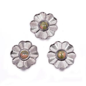 May include: Three flower-shaped decorative objects with a silver finish. Each flower has six petals and a central stone with green and brown hues. The objects are arranged on a white background.