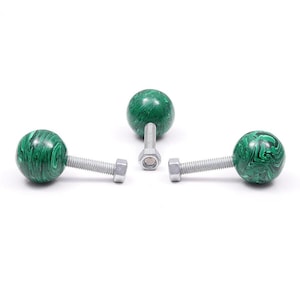 May include: Three decorative cabinet knobs with a green and black marbled pattern. Each knob features a spherical design attached to a silver-coloured bolt and nut. The knobs are arranged on a white background.