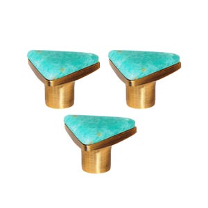 May include: Three cabinet knobs with a triangular, turquoise stone top and a brass base. The knobs have a modern design and are set against a white background. The turquoise stone has a speckled pattern.