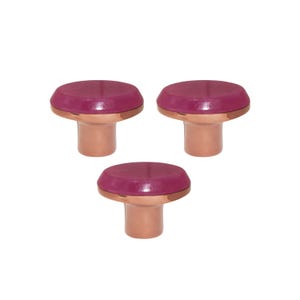 May include: Three cabinet knobs with a magenta top and copper base. The knobs are arranged in a triangular pattern. Each knob has a round, glossy magenta top and a copper-colored base.