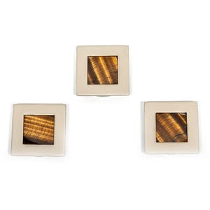 May include: Three square cufflinks with a silver frame, each featuring a square of tiger's eye stone. The tiger's eye displays a brown and gold striped pattern. The cufflinks are set against a white background.