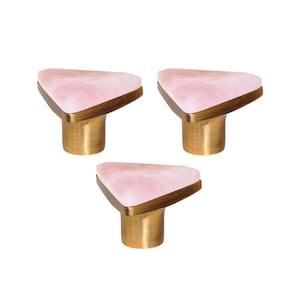 Pode incluir: Três puxadores de armário com um tampo triangular de pedra rosa marmorizada, emoldurado por metal dourado. Os puxadores têm uma base cilíndrica dourada. Estes puxadores decorativos são ideais para adicionar um toque de elegância aos móveis.