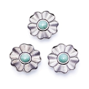 Puede incluir: Tres objetos decorativos plateados con forma de flor con una piedra central redonda de color verde claro. Los pétalos tienen una textura acanalada. Los objetos están dispuestos sobre un fondo blanco.