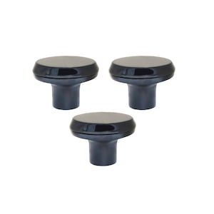 Puede incluir: Tres pomos de armario de color gris oscuro con una parte superior redondeada y una base cilíndrica. Los pomos tienen un acabado brillante y están dispuestos en un patrón triangular sobre un fondo blanco. Adecuados para cajones y armarios.