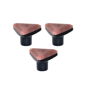 Può includere: Tre pomelli decorativi per mobili. Ogni pomello presenta una parte superiore triangolare, maculata, marrone rosata con un bordo nero, montata su una base cilindrica blu navy scuro. I pomelli sono su uno sfondo bianco.