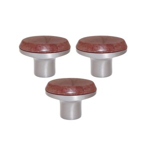 Può includere: Tre pomelli per mobili con base argentata spazzolata e parte superiore circolare marrone rossiccio. I pomelli hanno un design semplice e moderno, adatti per cassetti o ante di armadi. I pomelli sono su sfondo bianco.