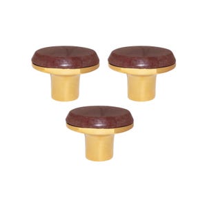 Può includere: Tre tappi per bottiglie con una parte superiore marrone e circolare e una base dorata. I tappi sono disposti a triangolo su sfondo bianco. Il design è semplice ed elegante, adatto alle bottiglie di vino.