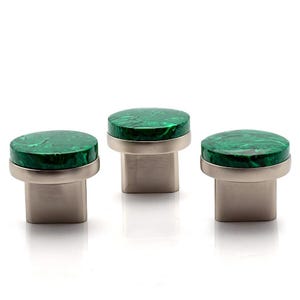 May include: Three cabinet knobs with a round, marbled green top and a brushed silver base. The knobs are evenly spaced against a white background. The green top has a swirling pattern.