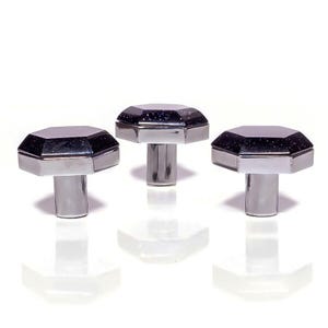 Pode incluir: Três puxadores decorativos para armários com base prateada e topo facetado azul escuro com inclusões brilhantes. Os puxadores estão dispostos em fila sobre um fundo branco.