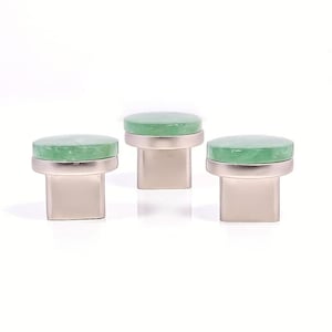 Può includere: Tre pomelli per mobili con una parte superiore circolare verde chiaro e una base rettangolare color argento. Le manopole sono disposte in fila su uno sfondo bianco. Le parti superiori verdi hanno un aspetto leggermente strutturato.