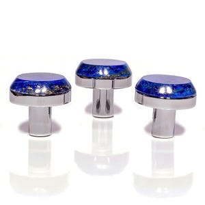 May include: Three silver-coloured mushroom-shaped objects with a blue and gold speckled top. The objects have a polished, reflective surface and are arranged in a row against a white background. The design is symmetrical and elegant.