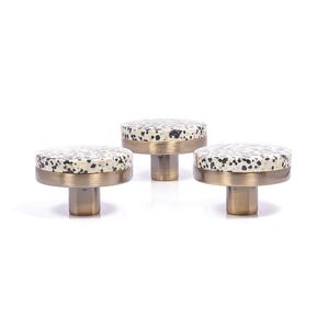 May include: Three cabinet knobs with a speckled, off-white and black top, a brass-coloured rim, and a brass-coloured stem. The knobs are arranged in a row against a white background. These knobs are ideal for adding a touch of elegance to any cabinet or drawer.