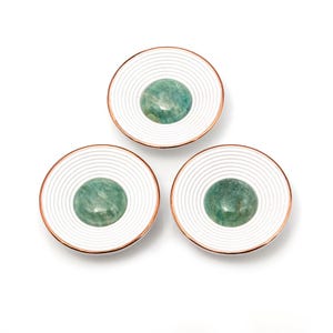 Puede incluir: Tres tiradores decorativos para armarios. Cada tirador presenta una cara blanca estriada con un borde color cobre y una piedra verde redondeada en el centro. Los tiradores están dispuestos en un patrón triangular sobre un fondo blanco.