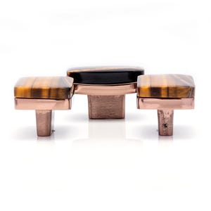 Può includere: Tre pomelli decorativi per mobili. I pomelli presentano una pietra rettangolare occhio di tigre incastonata in una base di metallo color rame. Il pomello centrale ha una striscia nera. Adatti per mobili e arredamento.