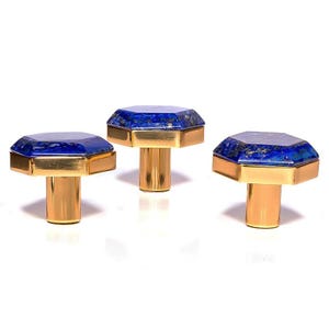 Könnte beinhalten: Drei dekorative Schrankknöpfe mit achteckigen blauen Edelsteinaufsätzen und goldfarbenen Metallsockeln. Die Knöpfe sind in einer Reihe angeordnet und präsentieren ihr Design und ihre Verarbeitung.