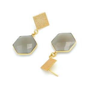 May include: A pair of gold-toned earrings with a geometric design. Each earring features a textured square stud, a gray, faceted, hexagonal stone, and a smaller textured gold rectangle. The earrings are set against a white background.
