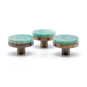 Op de afbeelding: Drie decoratieve kastknoppen met ronde, lichtgroene stenen toppen en antiek messing bases. De knoppen zijn in een rij gerangschikt tegen een witte achtergrond. Deze knoppen zijn perfect om een vleugje elegantie toe te voegen aan elk meubelstuk.