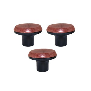 Può includere: Tre pomelli per mobili con base marrone scuro e parte superiore maculata marrone-rossastra. I pomelli sono rotondi e hanno un design semplice e moderno. Sono posti su uno sfondo bianco.