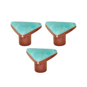 Könnte beinhalten: Drei Schrankknöpfe mit einer dreieckigen, türkisfarbenen Oberseite, kupferfarbenen Zierleisten und einem zylindrischen Kupfersockel. Die Knöpfe sind vor einem weißen Hintergrund angeordnet.