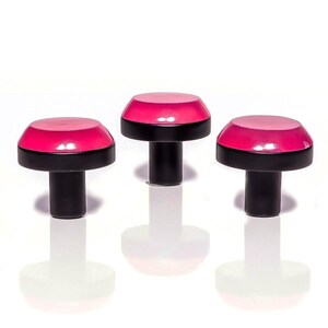May include: Three cabinet knobs with a bright pink top and a black base and stem. The knobs are arranged in a row against a white background. The knobs are approximately 4 cm in height, with their reflections visible below.