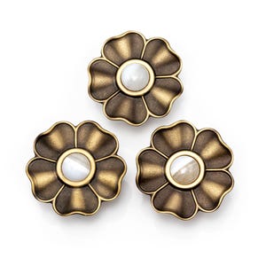 Puede incluir: Tres tiradores decorativos para armarios con forma de flor. Cada tirador presenta un diseño en forma de pétalo de color bronce con un centro blanco y circular. Los tiradores están dispuestos sobre un fondo blanco, mostrando sus intrincados detalles y acabado metálico.
