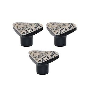Op de afbeelding: Drie kastknoppen met een driehoekige bovenkant met een gespikkeld patroon in beige en zwart. De knoppen hebben een zwarte, hoekige basis en een cilindrische steel. Deze decoratieve knoppen zijn geschikt voor meubels.