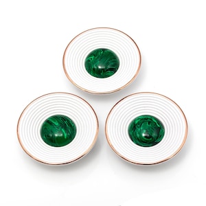 Puede incluir: Tres posavasos decorativos con un diseño blanco estriado y un borde color cobre. Cada posavasos presenta un centro verde vibrante y veteado. Los posavasos están dispuestos en un patrón triangular sobre un fondo blanco.