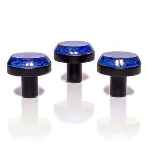 May include: Three cabinet knobs with a black stem and base. The top of each knob has a blue and silver speckled design. The knobs are arranged in a row against a white background, with their reflections visible.