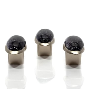 Könnte beinhalten: Drei Schrankknöpfe mit einer dunkelblauen, gesprenkelten, kuppelförmigen Oberseite und einem gebürsteten silbernen Sockel. Die Knöpfe sind in einer Reihe vor einem weißen Hintergrund angeordnet, wobei sich Reflexionen darunter zeigen.