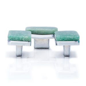 Könnte beinhalten: Drei Schrankknöpfe mit quadratischen, hellgrünen Steinplatten und silberfarbenen Metallsockeln. Die Knöpfe sind in einer Reihe angeordnet, wobei der mittlere Knopf leicht erhöht ist. Der Hintergrund ist weiß.