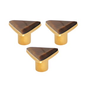 May include: Three cabinet knobs with a triangular tiger-eye stone design. The knobs have a gold-coloured base and a polished finish. Suitable for drawers, cabinets, or furniture. Each knob is approximately 3 cm in height.