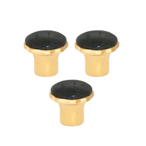 May include: Three cabinet knobs with a gold-coloured base and a dark, possibly black, oval top. The knobs have a decorative, scalloped edge where the top meets the base. The knobs are evenly spaced against a white background.