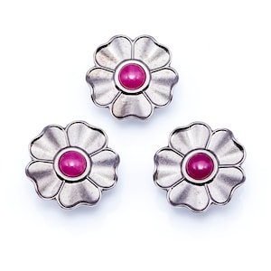 May include: Three silver-coloured flower-shaped buttons with a scalloped edge design. Each button features a vibrant, round, magenta-coloured centre. The buttons are arranged on a white background, showcasing their intricate details.