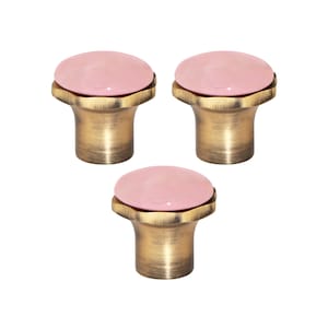 Pode incluir: Três puxadores de armário com um topo rosa arredondado e uma base cor de latão. Os puxadores têm um design decorativo em estilo antigo, adequado para projetos de móveis ou decoração de casa.