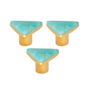 May include: Three cabinet knobs with a turquoise triangular stone set in a gold-coloured metal frame. The knobs have a cylindrical gold-coloured base. Ideal for furniture.