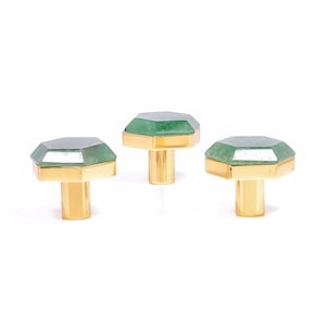 Op de afbeelding: Drie decoratieve kastknoppen met een facetgeslepen, smaragdgroene edelsteen top en een goudkleurige basis. De knoppen zijn in een rij gerangschikt tegen een witte achtergrond, wat hun elegante ontwerp en decoratiepotentieel laat zien.
