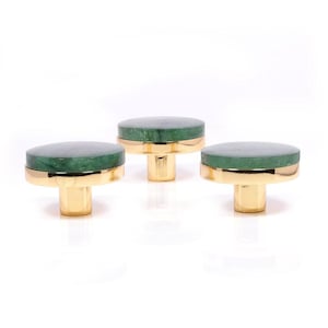 May include: Three decorative cabinet knobs. Each knob features a round, dark green stone top with a gold-colored band and a gold-colored cylindrical base. The knobs are arranged against a white background.