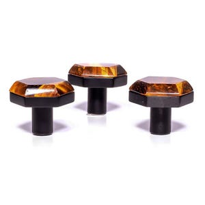 May include: Three cabinet knobs with an amber-coloured, faceted top and a black base and stem. The knobs are displayed against a white background, highlighting their design. The knobs are suitable for cabinets.
