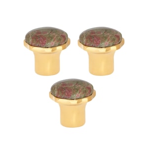 May include: Three cabinet knobs with a gold finish and a natural stone top. The stone has a mix of green and red hues. The knobs are designed for easy installation and add a touch of elegance to any furniture piece.
