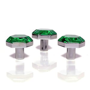 Può includere: Tre pomelli decorativi per mobili con una parte superiore in vetro verde smeraldo sfaccettato e una base in metallo color argento. I pomelli sono disposti a triangolo su sfondo bianco.